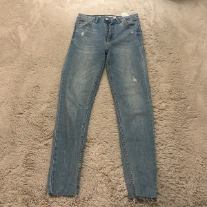 Ljusblå skinny jeans från Bershka - Säljer ett par ljusblå skinny jeans från Bershka i storlek 36. Jeansen har slitna detaljer, råa kanter vid bensluten och klassisk femficksdesign. Perfekta för en avslappnad och trendig look.