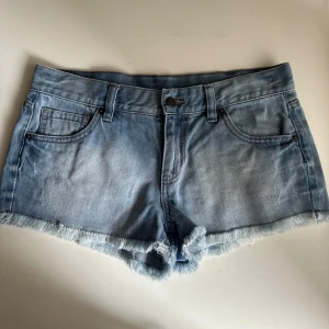 Blå jeansshorts med fransad kant - Snygga ljusblå jeansshorts med fransad kant och klassisk femficksdesign. Shortsen har låg midja, knapp och dragkedja framtill samt slitna detaljer för en cool look. Perfekta för varma sommardagar och chill häng med kompisarna.