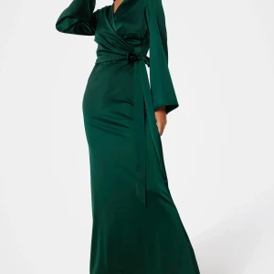 Grön omlottklänning i satin - Elegant lång grön satinklänning med omlott-design och v-ringning. Vida ärmar och midjeband. Helt ny, använd bara några timmar. Köpt för 900 kr.