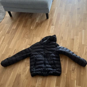 Svart Colmar pufferjacka med huva - Säljer en svart pufferjacka från Colmar med huva och dragkedja framtill. Jackan har två fickor med dragkedja och klassisk quiltad design. Perfekt för kalla dagar och riktigt snygg till streetwear-stilen. Priset går att diskuteras hör av er vid minsta fråga