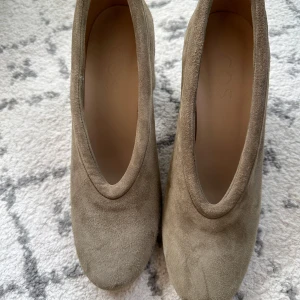 Beige mockapumps från COS - Chunky pumps från COS i beige mocka med rund tå och bred klack. Skorna har en stilren och minimalistisk design med mjuk ovandel i mocka och innersula i skinn. Perfekta för dig som gillar en clean look med lite edge.