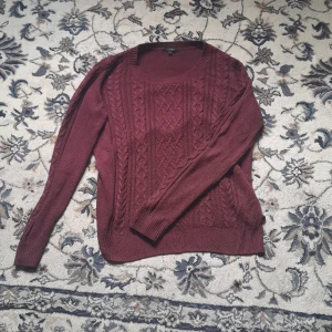 Vinröd stickad tröja från Lindex - Mysig vinröd stickad tröja från Lindex i storlek M. Tröjan har ett snyggt flätstickat mönster framtill, rund halsringning och långa ärmar. Perfekt för dig som gillar en klassisk men ändå trendig look under kyliga dagar.