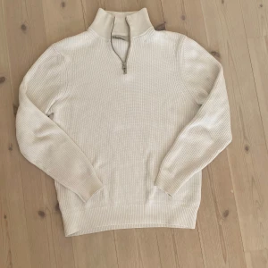 Beige ribbstickad half zip-tröja - Snygg beige ribbstickad tröja från Zara med half zip och hög krage. Tröjan har lång ärm och är tillverkad i mjuk bomull, perfekt för lager-på-lager. Enkel att matcha med jeans eller chinos för en clean look.