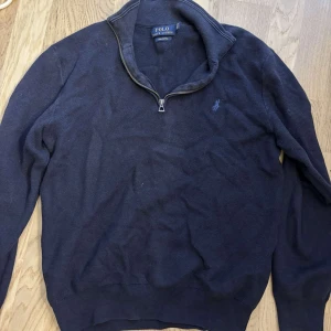 Marinblå half zip tröja Polo Ralph Lauren - Snygg marinblå långärmad tröja från Polo Ralph Lauren i mjuk pima bomull. Klassisk modell med half zip-dragkedja vid kragen och broderad logga på bröstet. Perfekt för en stilren och avslappnad look.