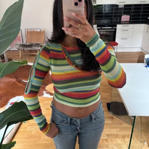 Randig croppad tröja - Färgglad croppad tröja från Stine Goya med randigt mönster i grönt, rött, blått, gult och orange. Långärmad och med vit outs vid ena armen. Från humana