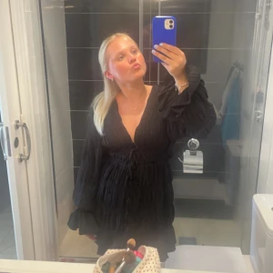 Svart klänning nakd x Moa Mattsson - Säljer en svart kort klänning med lite ”volanger” och en v-ringning. Klänningen har långa ärmar med volangdetaljer och knyt i midjan. Superfin och endast använd två gånger, kommer ej till användning längre! Nypris, 699kr