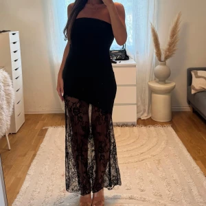 Svart lång klänning med spets - Säljer en svart axelbandslös långklänning med transparent spets nertill. Klänningen har en tight passform upptill och ett snyggt spetsmönster som ger en elegant vibe.  XS/S