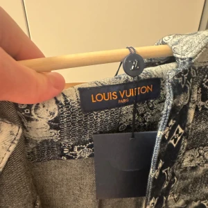 Louis Vuitton mönstrad skjorta blå/vit - Säljer en riktigt snygg Louis Vuitton skjorta med kort ärm och coolt blåvitt mönster med LV-loggor. Skjortan har klassisk krage, metallknappar framtill och är tillverkad i jeans. Perfekt för dig som vill sticka ut med exklusiv streetstyle. Den är aningen liten i storlek. Aldrig använd med tags kvar. Önskas fler bilder löser jag självklart de, kom med bud då allt är diskuterbart.