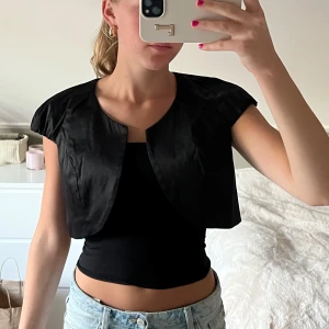 Svart bolero - Svart bolero med silkes aktigt tyg och knäppning i fram.