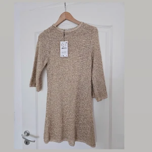 Beige stickad klänning från Zara - Säljer en beige stickad klänning från Zara i storlek S. Klänningen har en grovstickad struktur, rund hals och trekvartsärmar. Den är kort i modellen och har en mjuk, avslappnad passform som är både bekväm och snygg. Perfekt för dig som gillar en enkel men trendig look.