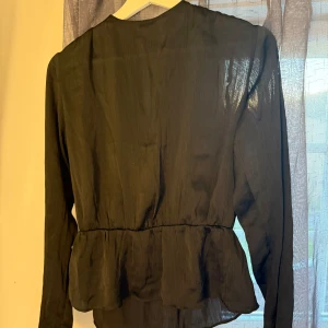 Blus  - Superfin svart blus från BIKBOK. Den har en superfin baksida med öppen rygg till viss del och sedan en fin knyt detalj i nacken. Funkar även att använda den bak och fram för att få en fin ”omlott” topp. Har även fina knappar på ärmarna. Kontakta gärna om du har fler frågor!🩷