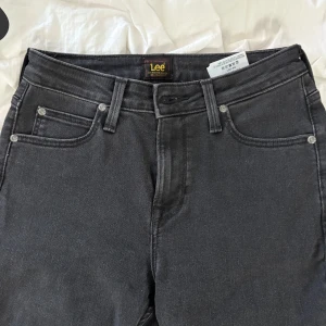 Svarta Scarlett High jeans från Lee - Snygga svarta Scarlett High jeans från Lee med klassisk femficksdesign och hög midja. Jeansen har raka ben och Lee-logga på bakfickan. Använda några gånger!