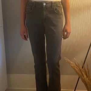 Grå bootcut jeans med hög midja - Snygga grå jeans med bootcut passform och hög midja. Klassisk femficksmodell med knapp och dragkedja framtill. Jeansen har raka ben som blir lite vidare nedtill och är tillverkade i mjukt denimtyg. Perfekta för dig som gillar en chill och stilren look.