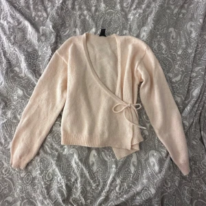 Beige omlottkofta från Lindex XS - Supermysig beige omlottkofta från Lindex i storlek XS. Koftan har långa ärmar, ribbade muddar och knytband i sidan för en snygg passform. Perfekt att slänga på sig när det är lite kyligt ute. Mjuk stickad känsla och enkel att matcha med jeans eller kjol.