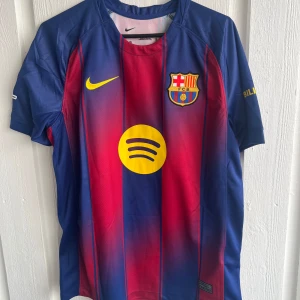 FC Barcelona Lamine Yamal #10 Nike tröja - Säljer en officiell FC Barcelona matchtröja från Nike med Lamine Yamal och nummer 10 på ryggen. Tröjan har klassiska blå och röda vertikala ränder, gula detaljer och klubbmärke på bröstet. Materialet är lätt och andas, perfekt för fotboll eller häng med kompisar.