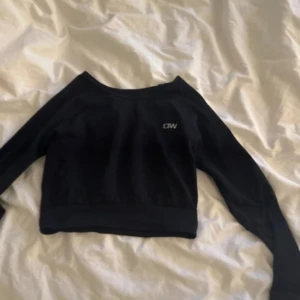 Svart croppad tröja från ICANIWILL - Svart långärmad croppad tröja från ICANIWILL med diskret logga på bröstet. Tröjan har en bred ribbad kant nedtill och är tillverkad i mjuk bomull och polyesterblandning. Perfekt för träning eller chill dagar. Snygg och enkel design som funkar till mycket.