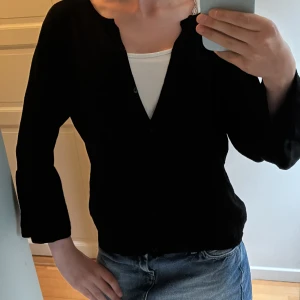 Svart kofta från Vero Moda med volymärm - Svart kofta från Vero Moda i storlek M. Är i storlek M men sitter ungefär som att det är storlek S. Koftan har långa volymärmar och knappar framtill. Rundad halsringning och mjukt material som känns skönt mot huden. Perfekt att slänga över en topp och jeans för en chill look.