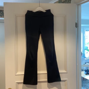 Svarta bootcut träningsbyxor från OTP Young - Snygga svarta bootcut byxor från OTP Young i stretchigt material. De har en hög midja och sitter skönt med en loose passform över benen. Perfekta för dig som gillar stilrena och bekväma byxor med lite utsvängda ben.