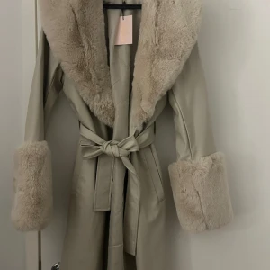 Beige pälsjacka från Missguided - Säljer en NEW beige pälsjacka från Missguided storlek s/36. Jackan har breda fuskpälsdetaljer vid krage och ärmslut, samt ett snyggt bälte i midjan för extra stilpoäng. Perfekt för dig som vill sticka ut med en lyxig och trendig look.