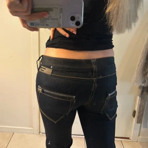 Lågmidjade Diesel Jeans - Säljer ett par svarta jeans från Diesel med snygga kontrastsömmar och coola dragkedjor på bakfickorna. Modellen har låg midja och bootcut-ben, vilket ger en schysst siluett. Har sytt på en spetskil på sidorna. I perfekt skick! Innerbens är ca 80 cm och mijemått är ca 80! (Strl: 26,32)💗
