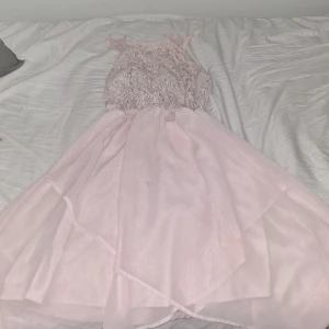 Ljusrosa spetsklänning från Lindex - Supersöt ljusrosa långklänning från Lindex med spets upptill och tunna axelband. Kjolen är i flera lager med ett skirt, flowy tyg som ger en drömmig känsla. Perfekt för dig som vill ha en romantisk look med fina detaljer och mjukt material. Stretchig i midjan