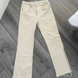 Beige ankel jeans från Zara, - Snygga beige jeans från Zara i rak modell med fransad kant vid benslut. Klassisk femficksdesign och hög midja. Tillverkade i mjuk bomull med dragkedja och knapp framtill. Perfekta för dig som gillar clean och stilren look.
