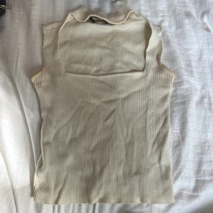 Ribbad polotopp i beige från Bershka - Säljer en beige ribbad polotopp från Bershka i storlek M. Toppen är ärmlös med hög krage och har en slim passform som sitter snyggt mot kroppen. Perfekt att styla med jeans eller kjol för en clean look.