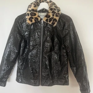 Svart jacka med leopardkrage - Cool svart jacka från Modström med glansig finish och dragkedja framtill. Kragen är i mjuk fuskpäls med leopardmönster som ger jackan en unik vibe. Långärmad och med normal passform, perfekt för dig som vill sticka ut.