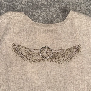 Beige stickad väst Zadig & Voltaire - Beige stickad väst från Zadig & Voltaire med ett snyggt vingmönster i paljetter/stenar på ryggen. Så snygg och unik men kommer tyvärr inte till användning. Storlek M men passar S och endast använd fåtal gånger!❤️‍🔥 
