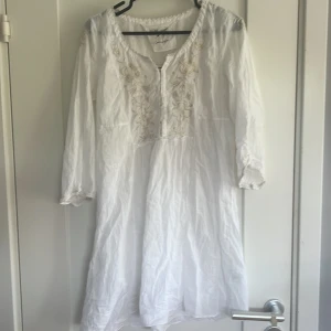 Vit Odd Molly långklänning med broderi - Supersöt vit långärmadklänning från Odd Molly med ljusa blommiga broderier framtill och diskreta broderade detaljer över hela klänningen. Långärmad och tillverkad i mjuk bomull, perfekt för sommarens alla tillfällen. Snygg v-ringning och romantisk känsla. Det är en kanska kort klänning(dvs inte över knäna)