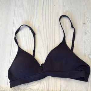 Svart triangelformad bh - Svart bh med triangelformade kupor och justerbara axelband. Bh-n har hak- och hyskknäppning bak och är tillverkad i mjukt, stretchigt material som sitter skönt mot kroppen. 