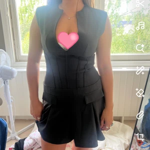 Grå kort klänning med markerad midja - Snygg grå klänning med kort längd och markerad midja. Klänningen har breda axlar, är ärmlös och har en djup v-ringning framtill. Kjoldelen är lätt utsvängd med fickdetaljer och dragkedja i ryggen. Passar en M