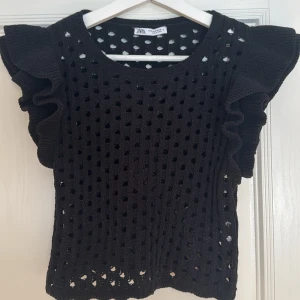 Svart stickad/virkad tröja med volangärmar från Zara - Snygg svart stickad tröja från Zara med hålmönster och volangärmar. Modellen är lite kortare. Storlek S men passar mer som XS. Mycket bra skick använd endast 1 gång. Köpt för 259kr