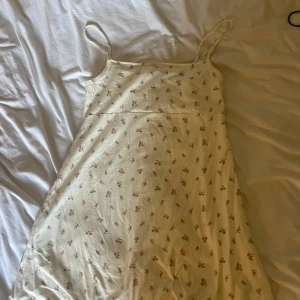 Blommig ljus kortklänning med smala axelband - Supersöt ljus kortklänning med smala axelband och ett gulligt blommigt mönster i rosa och grönt. Klänningen har en mjuk, lätt A-linjeform och är perfekt för varma dagar. Materialet känns som bomull och är riktigt skönt mot huden.