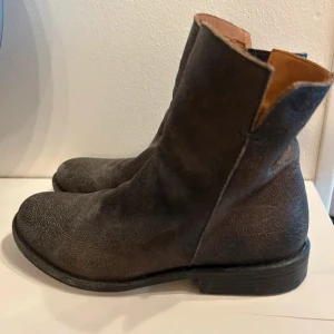 Bruna boots från Fiorentini+Baker - Säljer ett par snygga handgjorda bruna boots från Fiorentini+Baker i äkta skinn. Modellen har rund tå, platt sula och coola dragkedjor med metallring på sidan. Insidan är fodrad i ljusbrunt läder och yttermaterialet har en rå, vintagekänsla. Nypris 3.200:- 