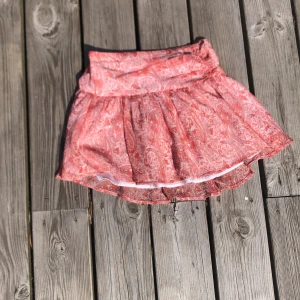 Rosa mönstrad kortkjol från Gina Tricot - Supersöt kortkjol från Gina Tricot i rosa och vitt med ett detaljerat paisley-inspirerat mönster. Kjolen har en volangig form och resår i midjan för skön passform. Perfekt för dig som gillar färg och mönster!