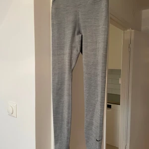 Nike Dri-Fit grå leggings S - Snygga grå Nike Dri-Fit leggings i storlek S. De har en slim och tight passform med hög midja och är gjorda i ett mjukt, stretchigt syntetmaterial som andas. Diskret Nike-logga vid benet. Supersköna