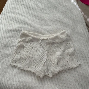 Vita stickade shorts med snörning - Säljer ett par vita stickade shorts med snyggt hålmönster och vågig kant. De har en midja med snörning och är perfekta för chill dagar eller sommarhäng. Mjukt material och riktigt skön passform, passar dig som gillar en unik och cozy stil.