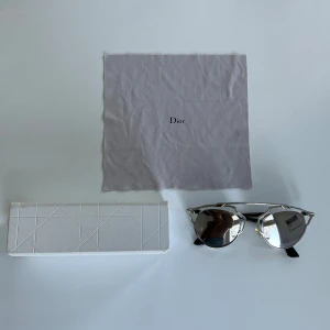 Dior solglasögon - Säljer ett par snygga Dior solglasögon med spegelblanka, runda linser och futuristisk silverfärgad metallram. Svarta skalmar med CD-detalj på sidan. Kommer med originalfodral och putsduk.