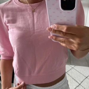 Ljusrosa croppad sweatshirt - Säljer en ljusrosa croppad sweatshirt med rund hals och puffade långärmar. Tröjan är i mjuk bomull och har ribbade muddar vid ärmslut och nederkant. Perfekt för dig som gillar en söt och chill stil.
