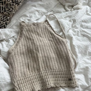 Beige stickad linnetopp från Hollister - Supersöt beige stickad linnetopp från Hollister med snyggt virkat mönster och knytband med tofsar i nacken. Toppen har en croppad passform och är ärmlös, perfekt för varma dagar. Materialet är mjukt och luftigt, och kanten har en fin virkad detalj.