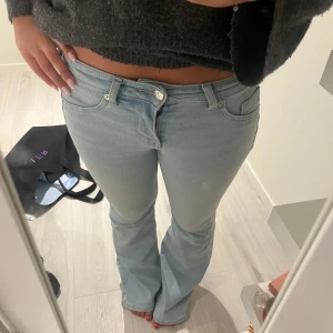Ljusblå bootcut jeans - Säljer ett par ljusblå jeans med bootcut passform och klassisk femficksdesign. Jeansen har låg midja och är tillverkade i mjukt denim-material. Perfekta för dig som gillar en chill och retro vibe. Passar dig som vill ha en snygg siluett med lite utsvängda ben.