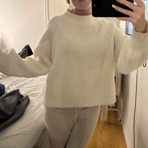 Vit ribbad stickad tröja med hög krage - Säljer en vit stickad tröja med ribbad struktur och hög krage. Tröjan har en loose passform och långa ärmar som ger en chill och cozy vibe. Perfekt att slänga på sig när det är kallt ute. Superenkel att styla med jeans eller mjukisbyxor.