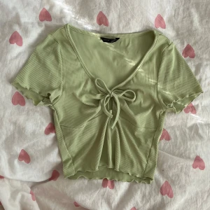 Ljusgrön croppad topp med knytning - Ljusgrön croppad topp från SHEIN i strl XS med ribbad struktur och v-ringning. Toppen har korta ärmar med vågig kant och knytning framtill!💞       OBS! Säljer en i svart också 