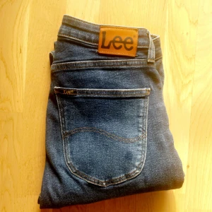 Blå skinny jeansen från Lee - Snygga blå jeans från Lee med klassisk femficksdesign och Lee-logga på bakfickan. Jeansen har smal passform och är tillverkade i mjukt denimtyg med lite stretch. De har normal midja och är perfekta för dig som gillar en modern och stilren look.