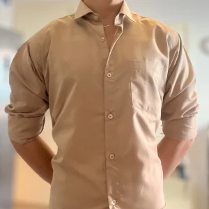 Beige skjorta från Tetis Brand - Snygg beige skjorta från Tetis Brand i storlek L. Klassisk modell med krage, bröstficka och knappar framtill. Långärmad och tillverkad i mjuk bomull som känns skön mot huden. Perfekt för dig som gillar stilrena och enkla plagg.