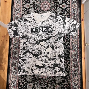 Kenzo svartvit grafisk t-shirt M - Kenzo t-shirt i storlek M med ett galet coolt svartvitt grafiskt mönster över hela plagget och stor logga på bröstet. T-shirten har rund hals och korta ärmar. Materialet är mjuk bomull som känns skönt mot huden. Perfekt för dig som gillar statement-plagg och streetstyle.