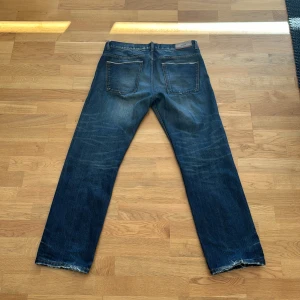 Blå jeans från HUGO - Säljer ett par klassiska blå jeans från HUGO med raka ben och snygga slitningar vid bensluten. Jeansen har fem fickor och röda detaljer på insidan av linningen. Perfekta för en avslappnad stil. Nypris på dessa är runt 1299, mitt pris 299! Pris går att diskuteras! Hör av er vid minsta lilla fundering🤗