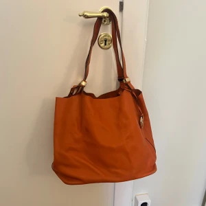 Mikael Kors handväska - Säljer denna väska ifrån Mikael Kors! Den är superbra om man har dator osv, den rymmer mycket! Stilren och härlig färg🧡