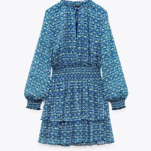 Blå mönstrad klänning från Zara - Supersnygg blå och grön mönstrad klänning från Zara med långa ärmar och smock i midjan. Klänningen har volangdetaljer på kjolen och knytning vid halsen. Den är i storlek L men skulle passa mer som en S/M 🫶🏼